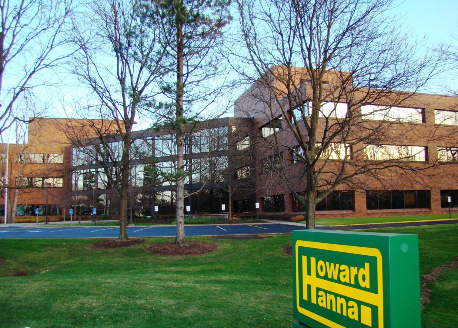 A brick building behind leafless trees and a lawn with a Howard Hanna sign. A brick building behind leafless trees and a lawn with a Howard Hanna sign.