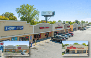 A strip mall with various stores and parked cars under a clear sky.